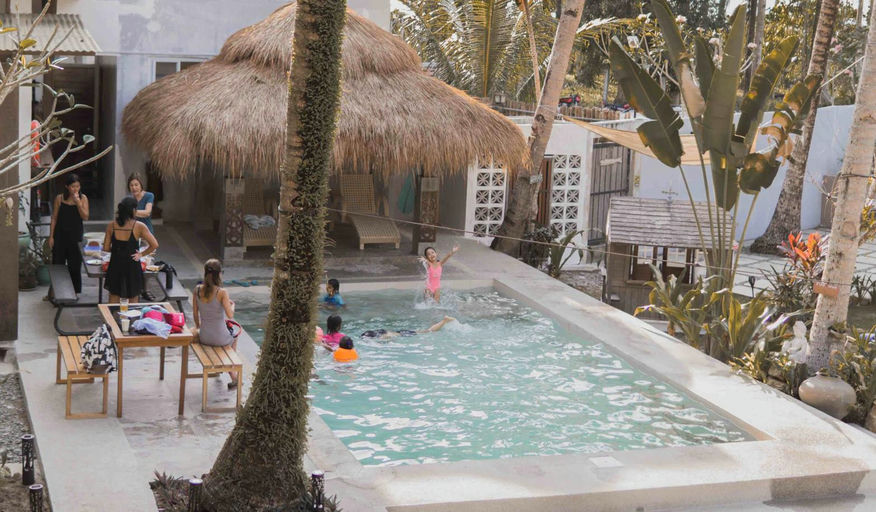 Guests, including children, enjoying the outdoor pool surrounded by palm trees at Kahana Baler in Cemento, Baler.