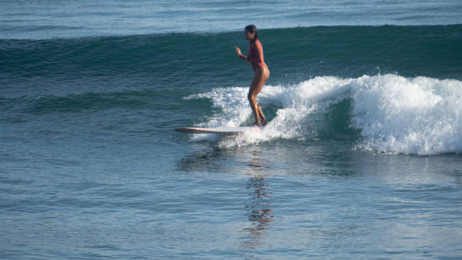 A surfer in a wetsuit rides a clean wave in clear blue water off the Baler coast during peak swell season.