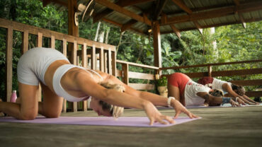 Group practicing yoga stretches on an open-air wooden deck at Kahana Baler, Cemento, Baler