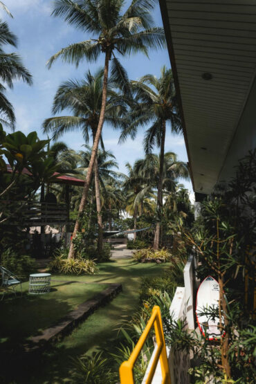 A surfboard leaning on the veranda rail looking out over the palm garden at Kahana Baler in Cemento, Baler