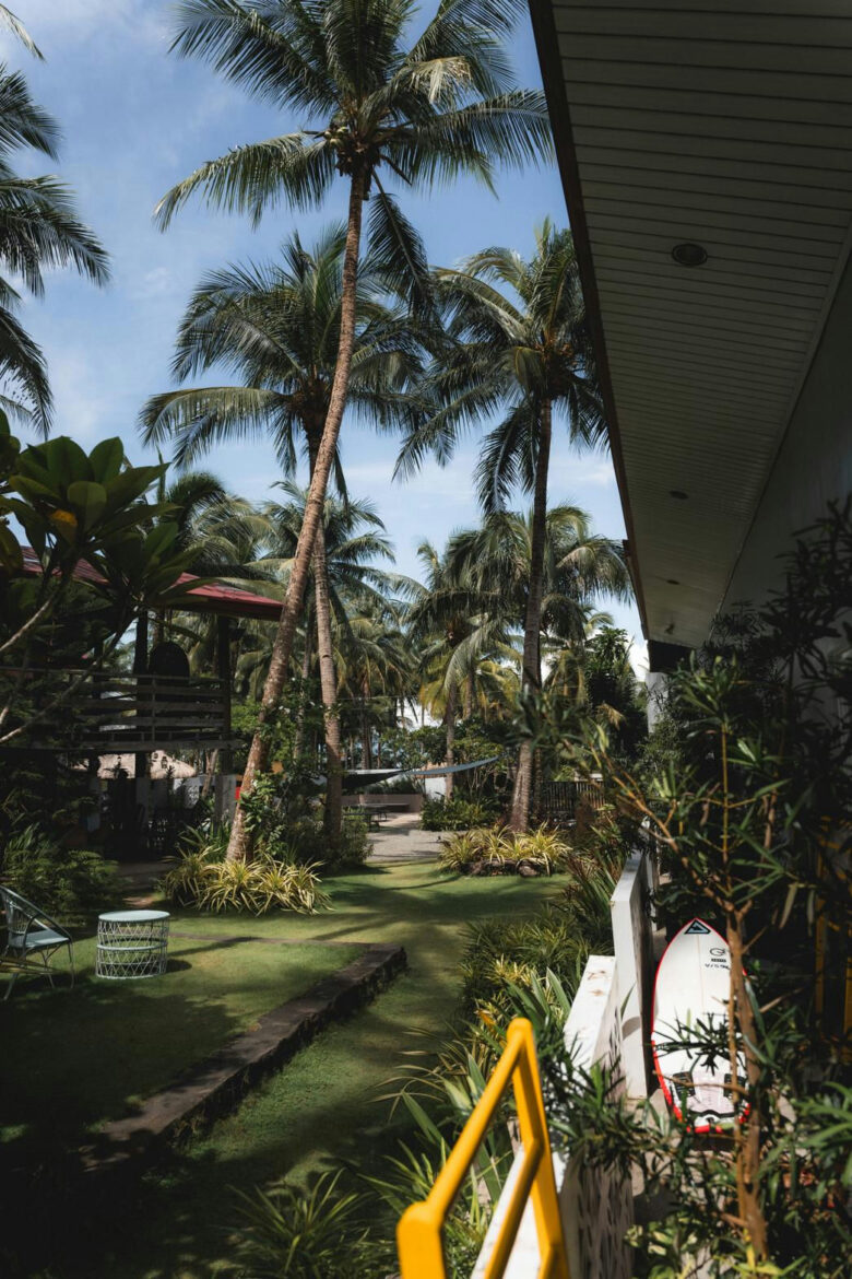 A surfboard leaning on the veranda rail looking out over the palm garden at Kahana Baler in Cemento, Baler