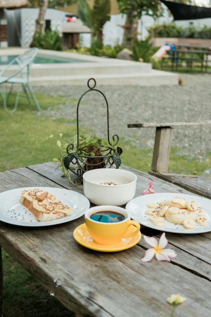 Coffee and toast on a wooden table by the pool and garden at The Shala Grounds cafe, Kahana Baler